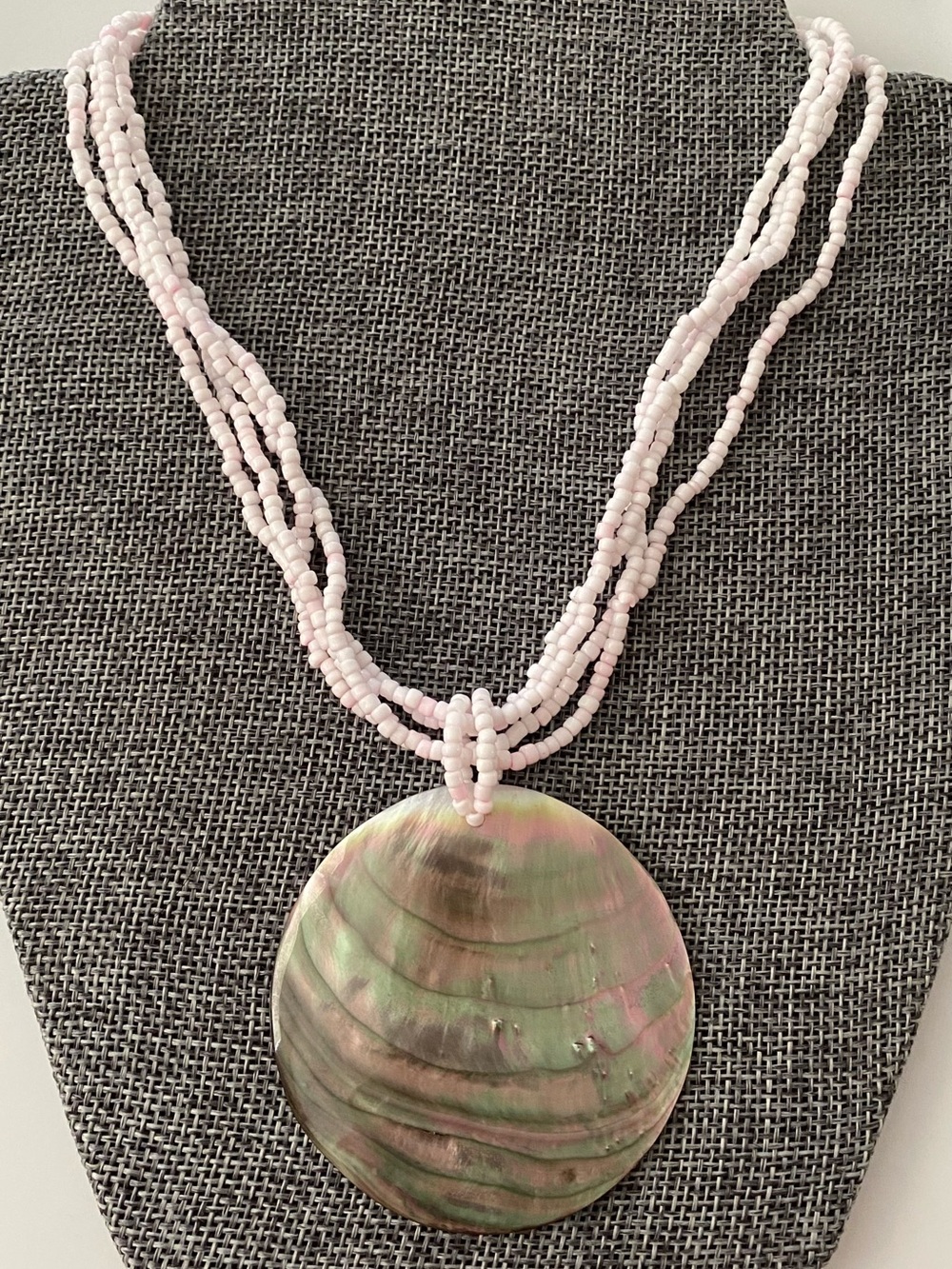 Multi-strand beaded necklace with a large abalone shell pendant.